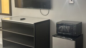 Una kitchenette con microondas, televisor montado en la pared y un mueble pequeño.