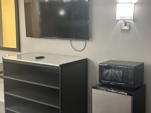 Una kitchenette con microondas, televisor montado en la pared y un mueble pequeño.