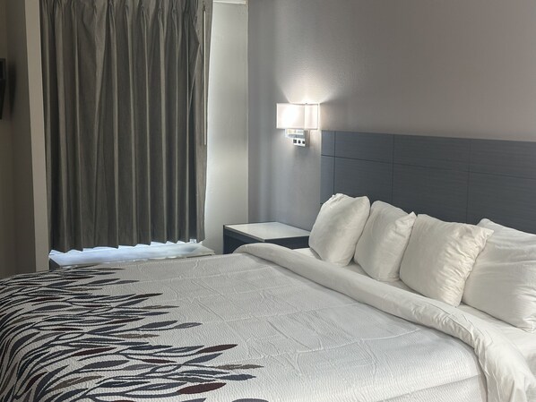 Una habitación de hotel con una cama grande, una mesita de noche, una lámpara de pared y un ventanal con cortinas.