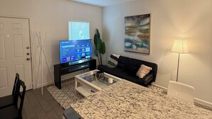 Espaço compacto com cozinha, mesa de jantar, sofá e televisão fixada na parede.
