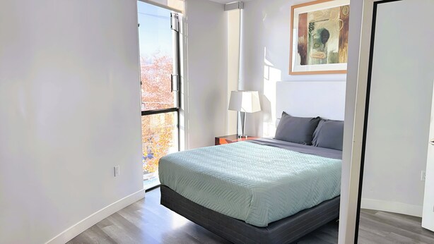 A bedroom with a bed, a nightstand, a lamp, and a painting on the wall.