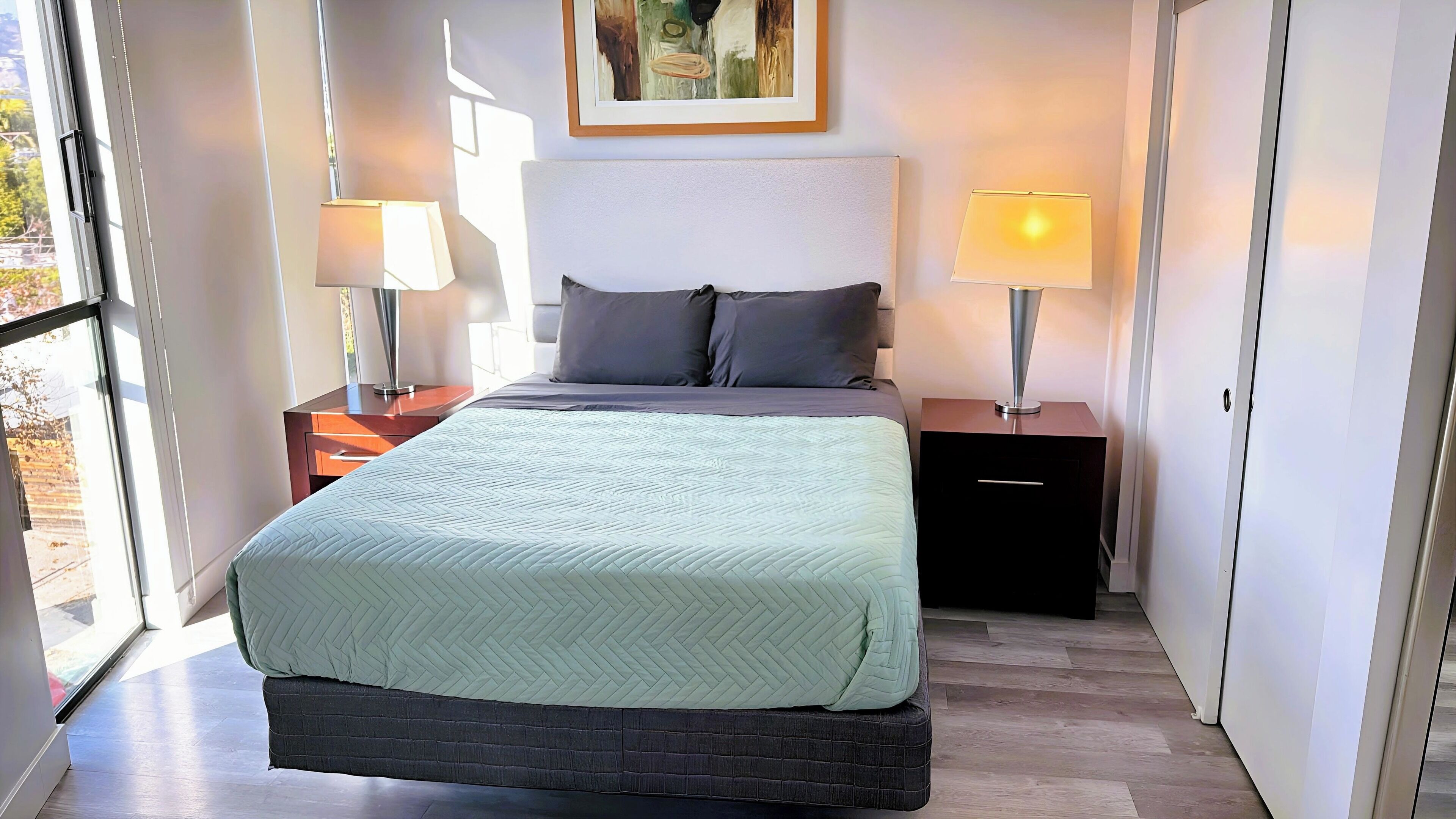 Une chambre bien rangée, avec un lit, deux tables de chevet et un tableau accroché au mur.