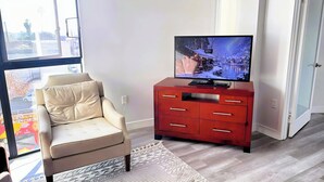 A living room with a beige armchair, a red TV stand with a flat-screen TV, and a patterned rug.