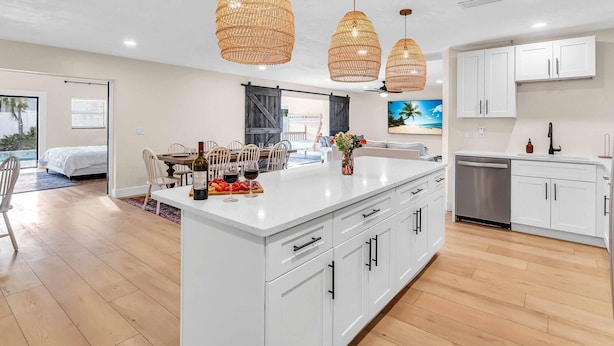 Una cocina moderna con muebles blancos, una isla central y tres lámparas colgantes de mimbre.