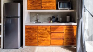A compact kitchen with a built-in refrigerator, wooden cabinets, a microwave, and a sink. - Seremonia Origen (Tulum)