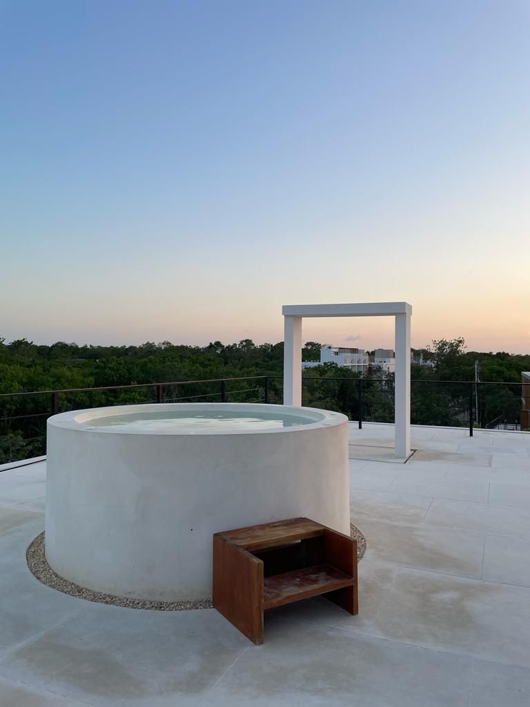 A rooftop terrace with a circular hot tub, a wooden bench, and a white structure.