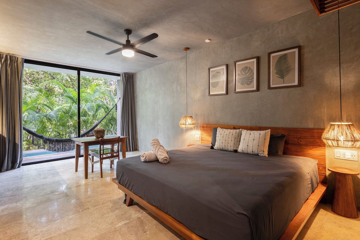 Une chambre dotée d’un grand lit, d’un ventilateur de plafond, d’un hamac et offrant une vue sur une végétation luxuriante.