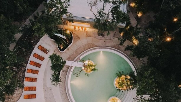 A circular pool with seating around it, surrounded by trees and a pathway. - Seremonia Origen (Tulum)