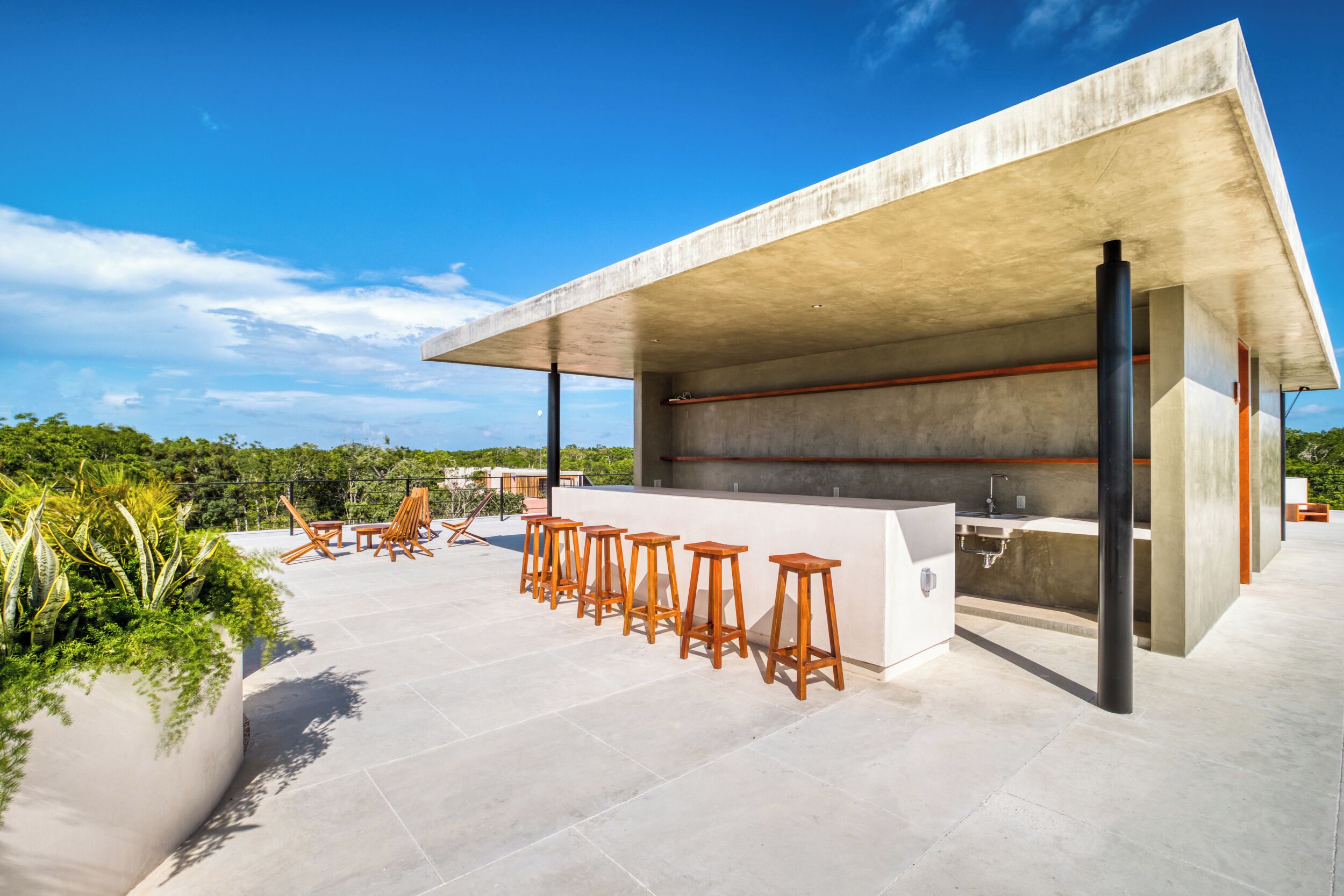 Un área de cocina exterior moderna con estructura de concreto, taburetes de bar y un lavamanos.