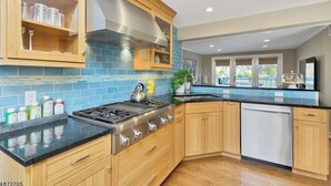 A modern kitchen with wooden cabinets, a stainless steel range hood, and a black countertop. - WORLD CUP LUXE–Walk to Train+Heated Pool & Spa-20 Min to Newark Airport-Sleep 10 (New Providence)