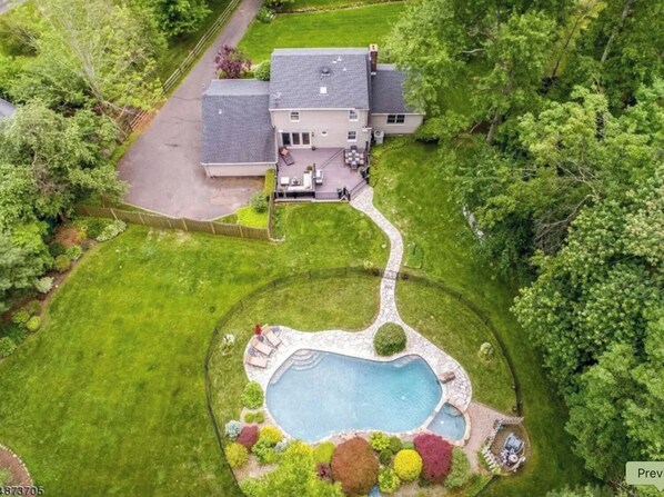 Ein Luftbild eines Hauses mit Swimmingpool, umgeben von einem gepflegten Rasen und Bäumen.