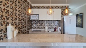 A kitchen with patterned wallpaper, a white countertop, a microwave, a refrigerator, and pendant lights. - COPIU0100 - Edifício Corsário (Salvador)