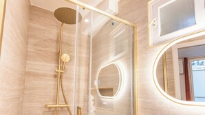 Ein modernes Badezimmer mit einer gläsernen Duschkabine, Marmorwänden und einem großen Spiegel mit goldener Rahmung.