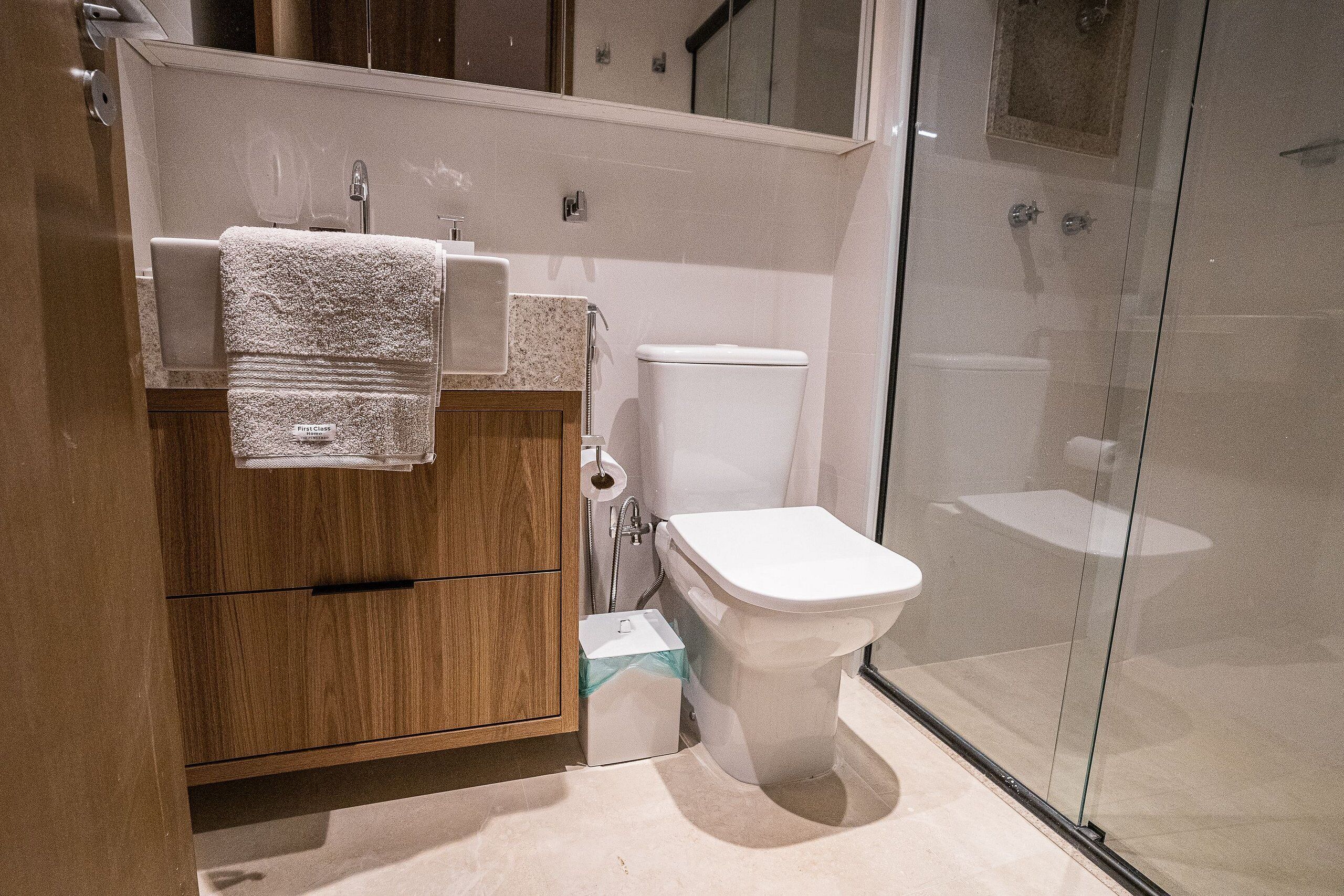A modern bathroom with a wooden vanity, a toilet, and a glass shower enclosure.