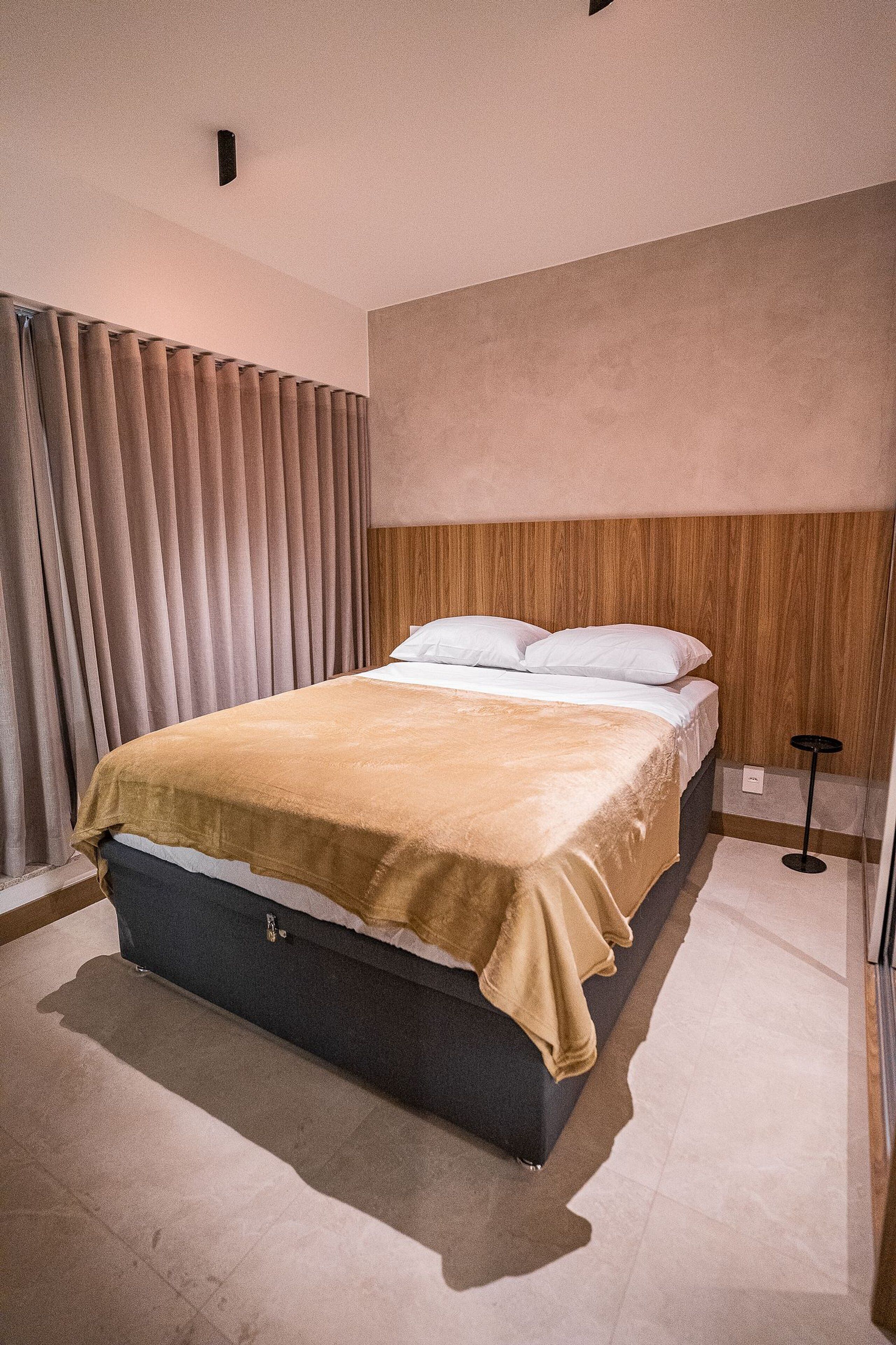 A modern bedroom with a bed, curtains, a wooden headboard, and a small bedside table.