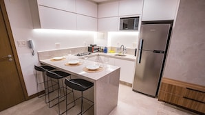 A modern kitchen with a central island, bar stools, a microwave, and a refrigerator. - Apartamento novo de alto padrão 223NW (Brasilia)