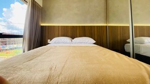 A hotel room with a bed, a large window with curtains, a view of a stadium, and a mirror on the wall. - Apartamento novo de alto padrão 223NW (Brasilia)