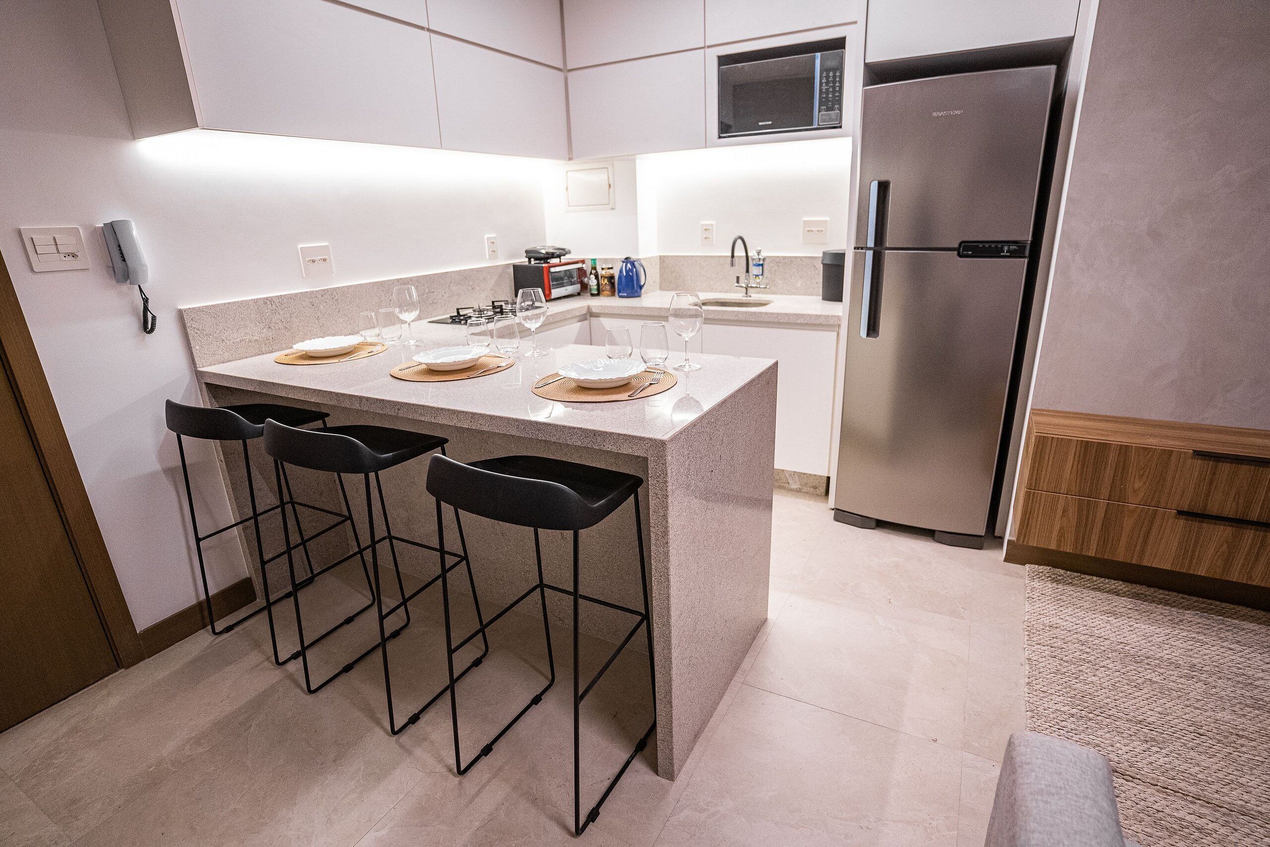 A modern kitchen with a central island, bar stools, a stainless steel refrigerator, and a microwave.