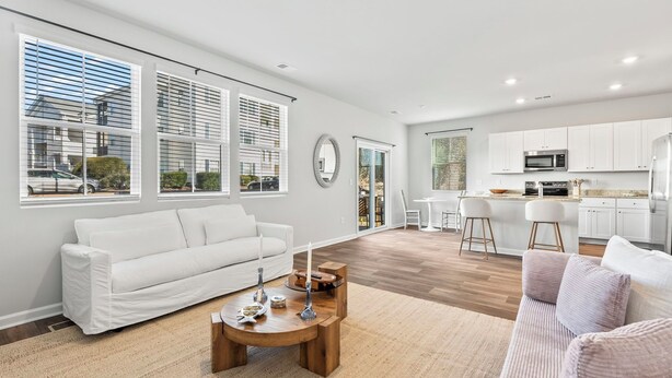 A modern living room with a white sofa, a wooden coffee table, and a kitchen area with white cabinets and appliances. - North Myrtle Beach Escape · Spacious 4BR Home (North Myrtle Beach)