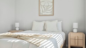 A bedroom with a bed, two nightstands, a wall-mounted artwork, and a window casting shadows. - North Myrtle Beach Escape · Spacious 4BR Home (North Myrtle Beach)