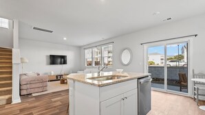 A modern kitchen with a central island, a dining area with a table and chairs, a sofa, and a TV mounted on the wall. - North Myrtle Beach Escape · Spacious 4BR Home (North Myrtle Beach)