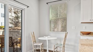 A modern kitchen with a white table and chairs, a window with blinds, and a view of the outside. - North Myrtle Beach Escape · Spacious 4BR Home (North Myrtle Beach)