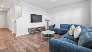 Ein modernes Wohnzimmer mit einem blauen Sofa, einem runden Couchtisch und einem flachbildfernseher, der an der Wand befestigt ist.