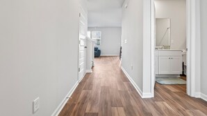 Ein Flur mit Holzdielen, weißen Wänden und einer Tür zu einem Badezimmer mit Spiegel und Waschbecken.
