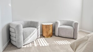 Une pièce avec deux fauteuils gris, une petite table d’appoint ronde en bois et un tapis à motifs.