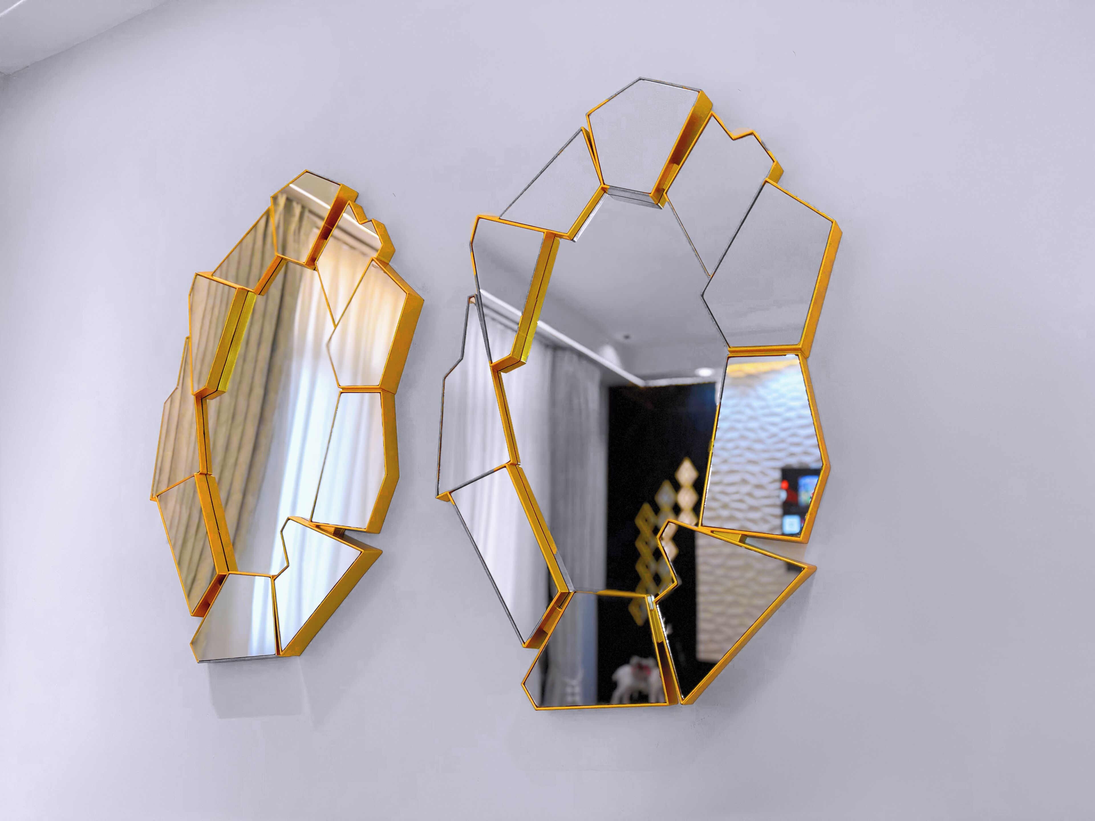 Two hexagonal mirrors with gold frames on a white wall.