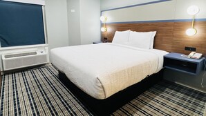 A hotel room with a large bed, a flat-screen TV, a bedside table with a phone, and a wall-mounted light fixture. - Americinn By Wyndham Rawlins (Rawlins)