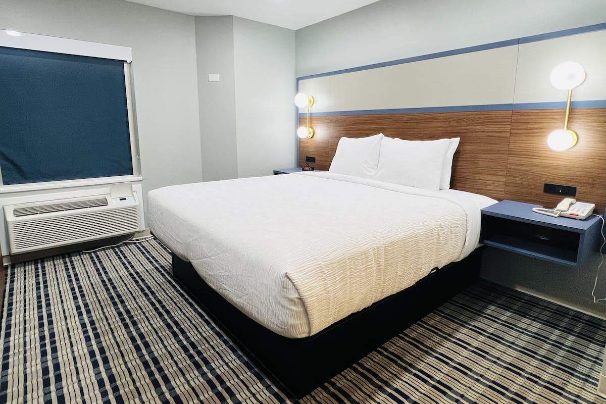 A hotel room with a large bed, a flat-screen TV, a bedside table with a phone, and a wall-mounted light fixture.