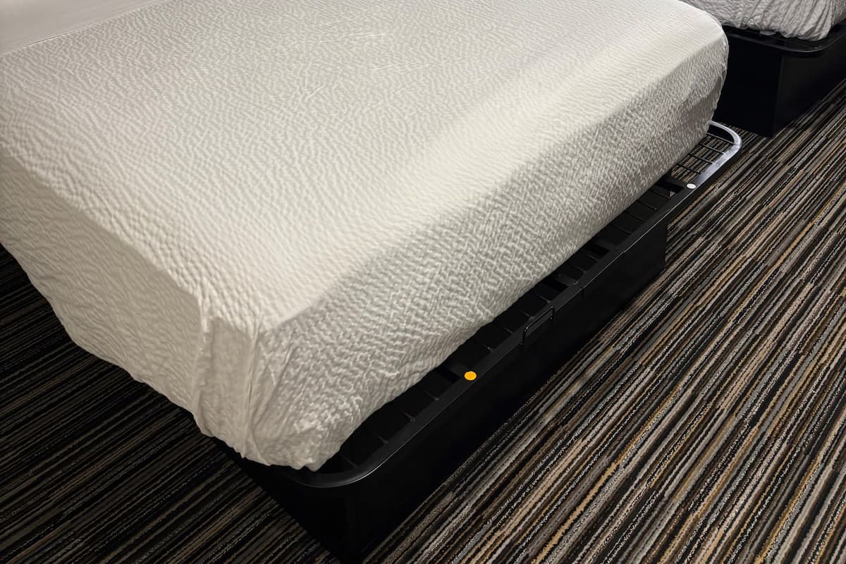 Une chambre d’hôtel avec deux lits, une table de chevet avec une lampe et une tête de lit ornée d’un motif géométrique.