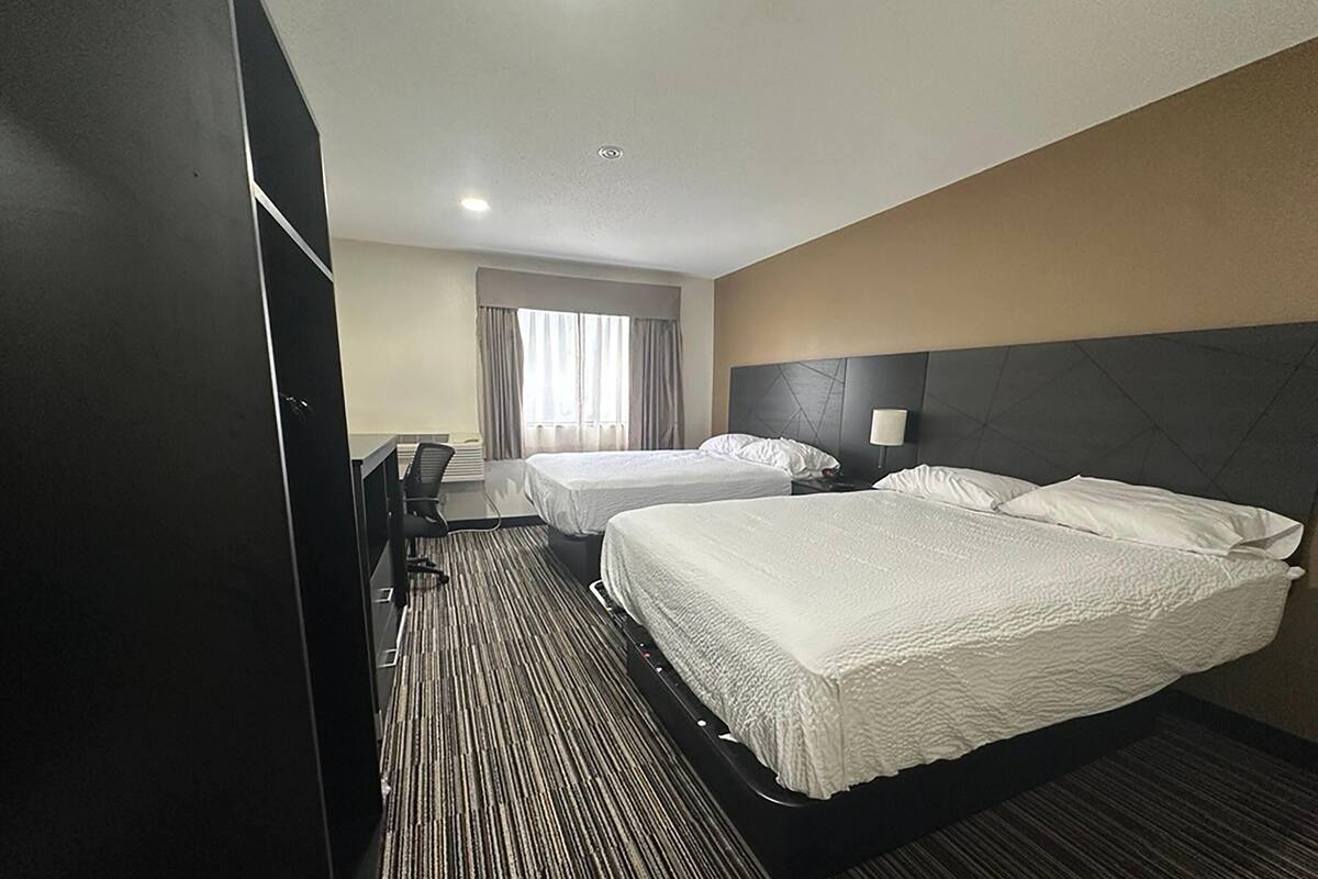Une chambre d’hôtel avec deux lits, un bureau et une fenêtre avec des rideaux.