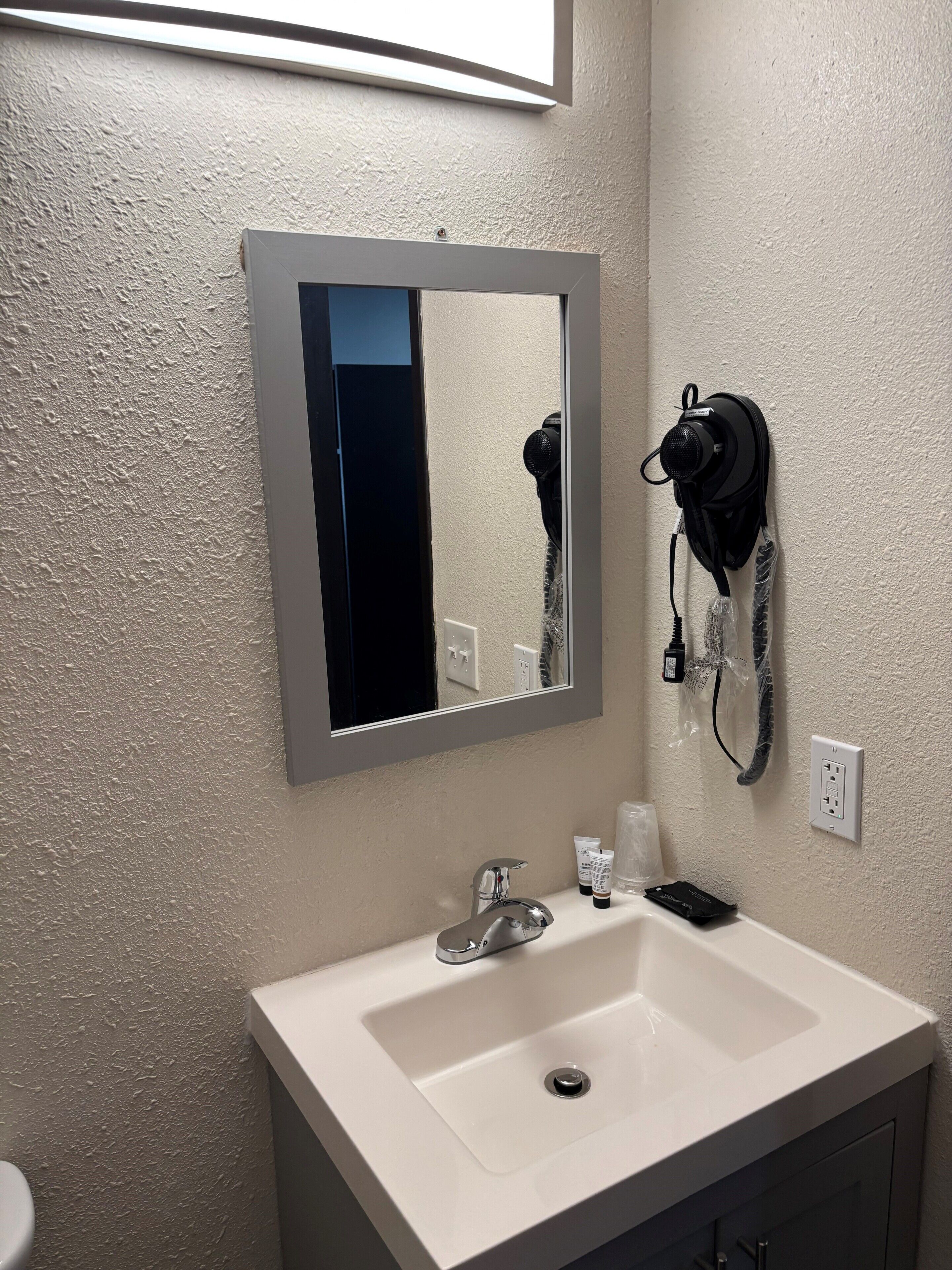 Une salle de bain avec un lavabo blanc, un miroir, un sèche-cheveux et des articles de toilette.