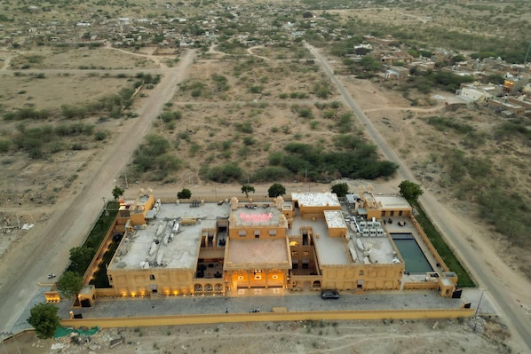 An aerial view of a large, yellow building with multiple sections, surrounded by a desert landscape. - Ramada By Wyndham Jaisalmer Barmer Road (Jaisalmer)