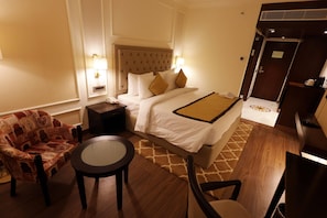 A hotel room with a bed, a chair, a small table, and a nightstand. - Ramada By Wyndham Jaisalmer Barmer Road (Jaisalmer)