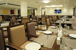 A hotel dining area with multiple tables set for guests, equipped with chairs, plates, cutlery, and glasses. - Ramada By Wyndham Jaisalmer Barmer Road (Jaisalmer)