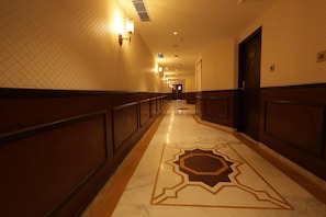 A hotel hallway with a marble floor, wall sconces, and a door at the end. - Ramada By Wyndham Jaisalmer Barmer Road (Jaisalmer)