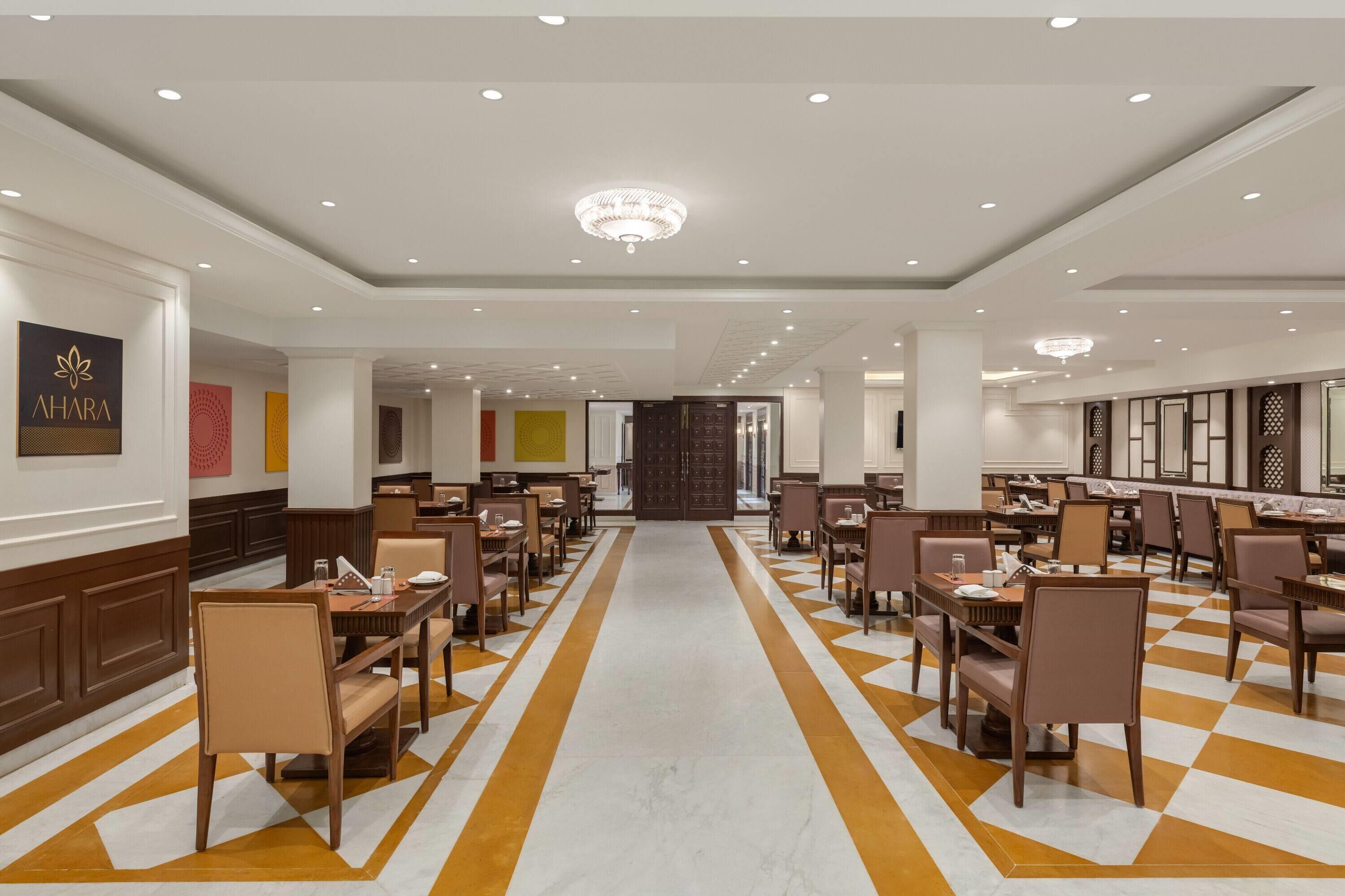 Amplia zona de comedor de hotel con varias mesas y sillas, un pasillo central y una araña.