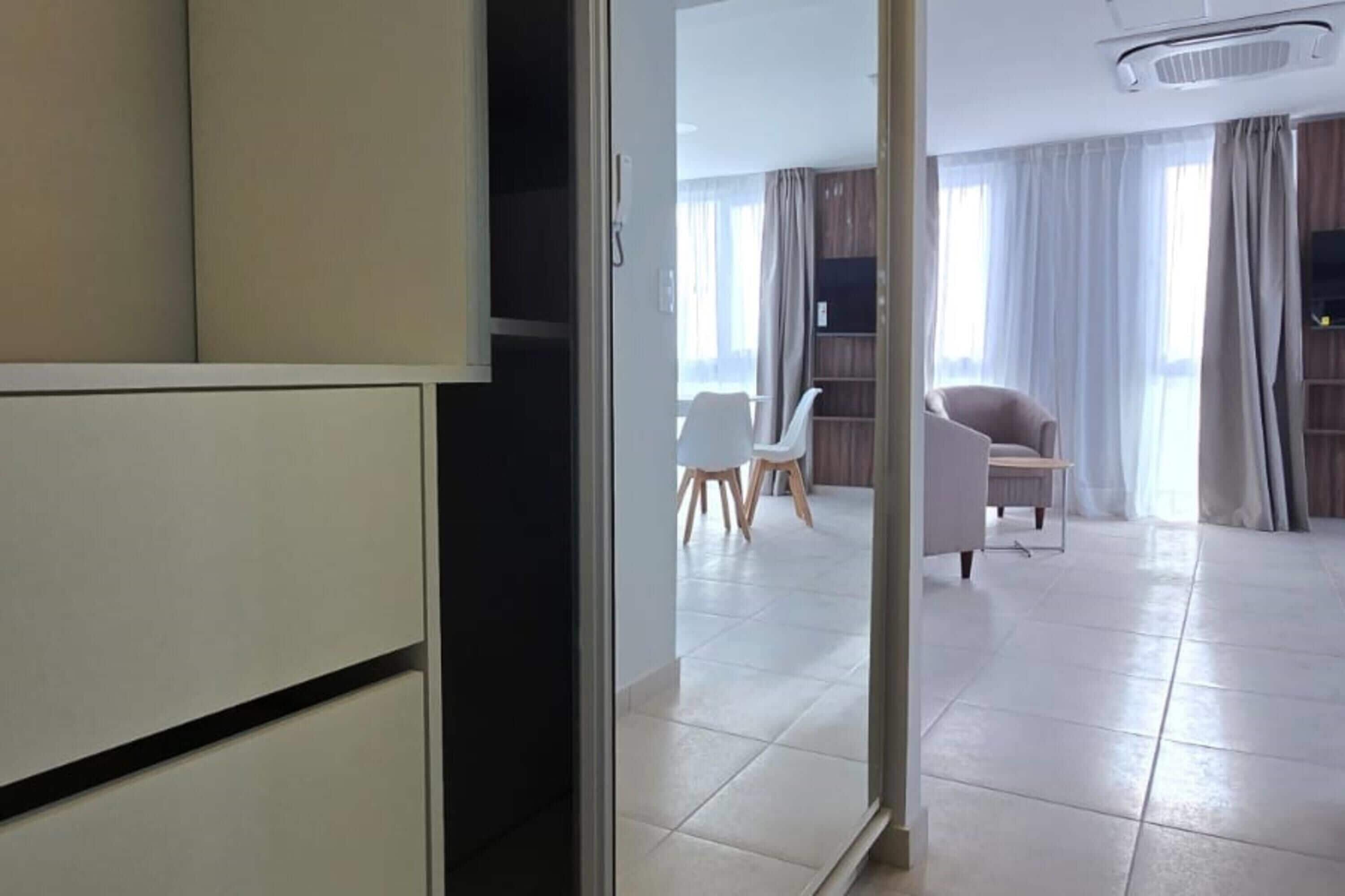 Un salon moderne avec un canapé blanc, une table à manger et des chaises, et un téléviseur fixé au mur.