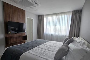 Hotellihuone, jossa on sänky, puupaneeliin kiinnitetty televisio, ikkuna verhoilla ja kattoilmanvaihtoaukko.