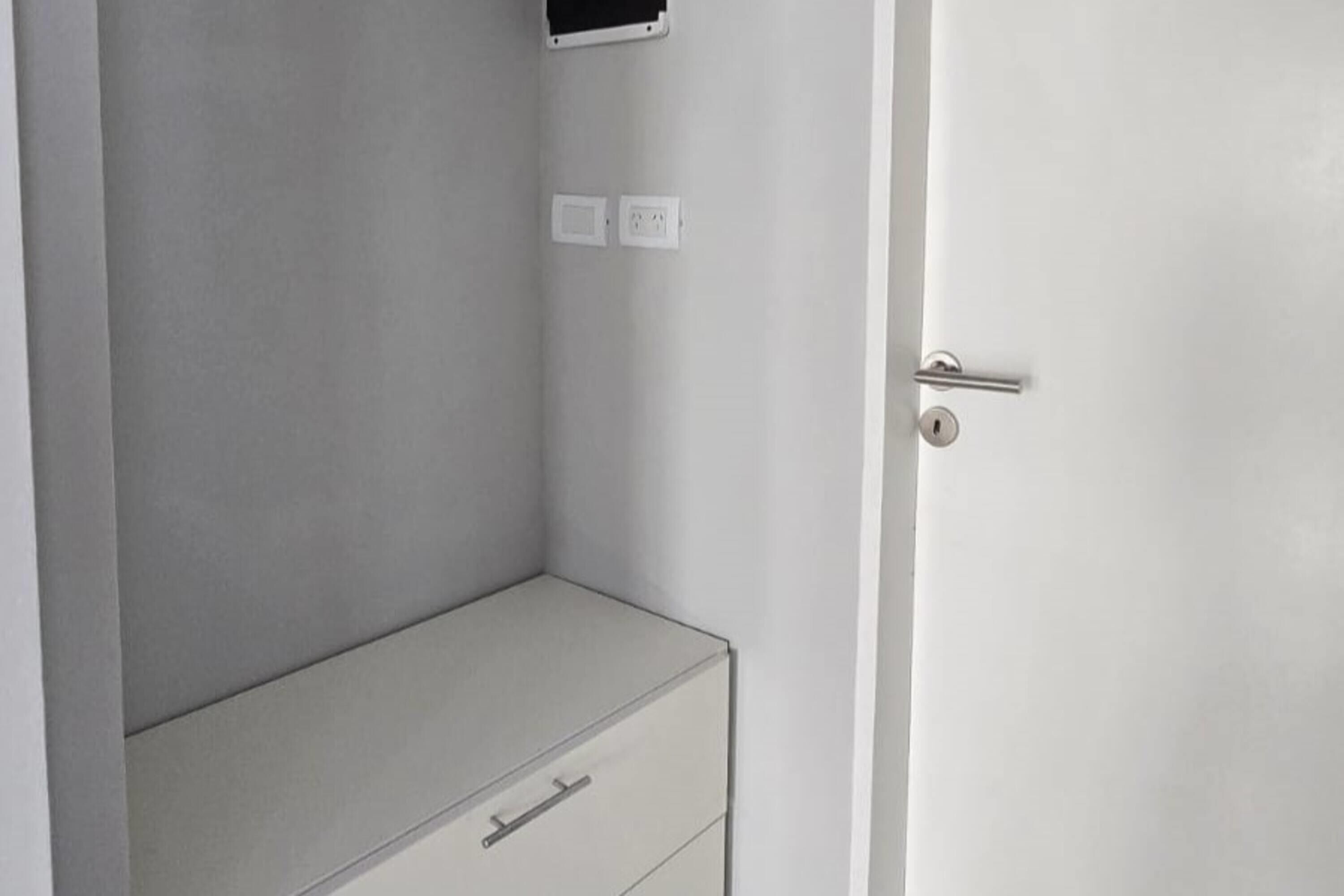 A white wardrobe with a handle, a door with a lock, and two electrical outlets on the wall.
