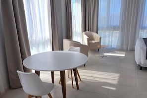 Moderni hotellihuone, jossa on pyöreä valkoinen pöytä, kaksi valkoista tuolia, pieni pyöreä pöytä ja valkoisilla tekstiileillä varustettu sänky.