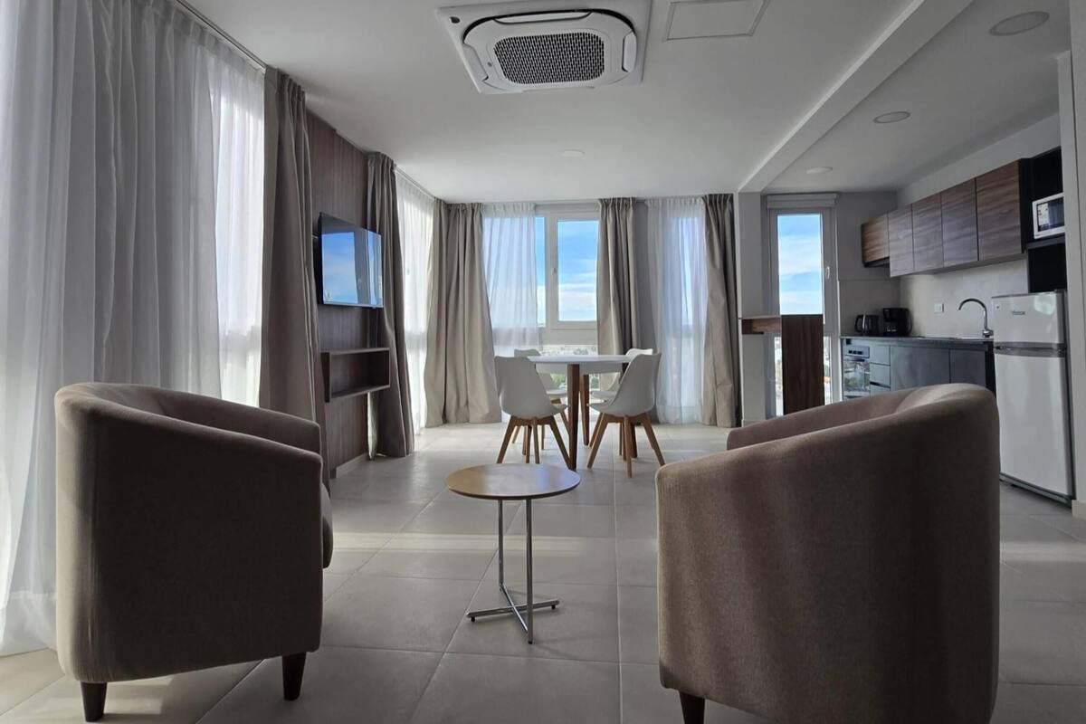 Quarto de hotel moderno com área de refeições, cozinha e televisão.