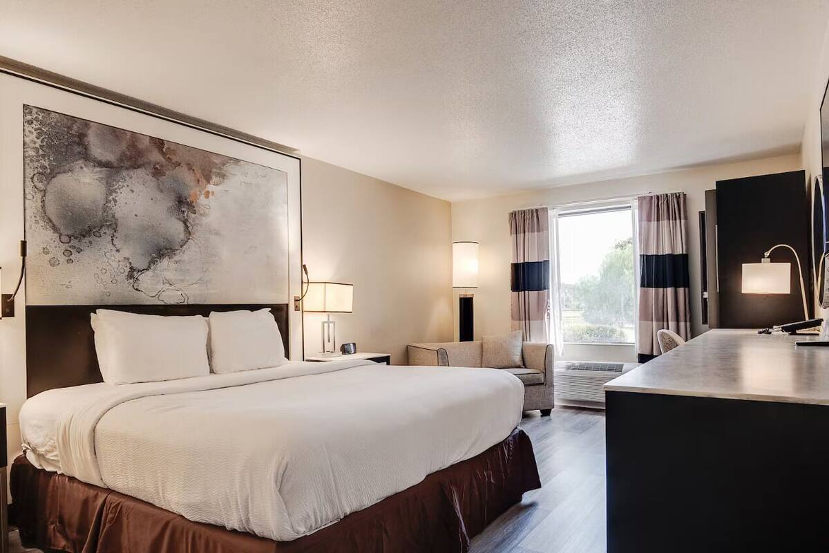 A hotel room with a large bed, bedside tables, a desk, and a large abstract painting.