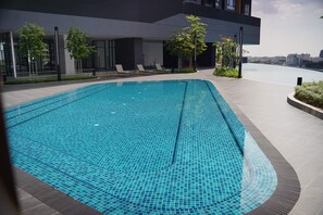 A modern outdoor swimming pool with a tiled surface, surrounded by lounge chairs and potted plants, with a view of a cityscape in the background. - Wyndham Grand I-City (Shah Alam)