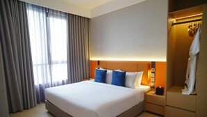 A modern hotel room with a large bed, a bedside table, a wardrobe, and a window with curtains.