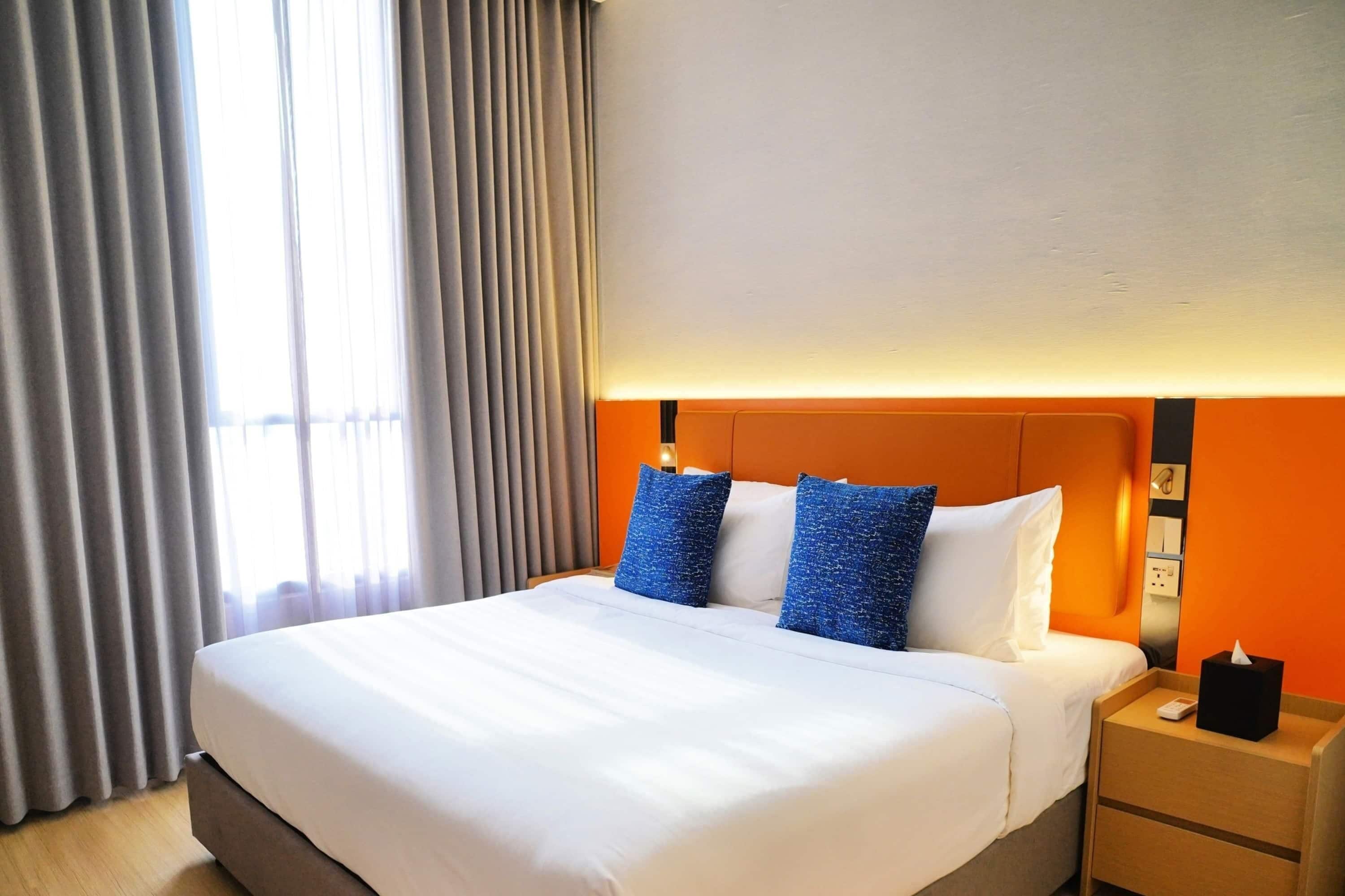 A hotel room with a large bed, a nightstand, and a window with curtains.