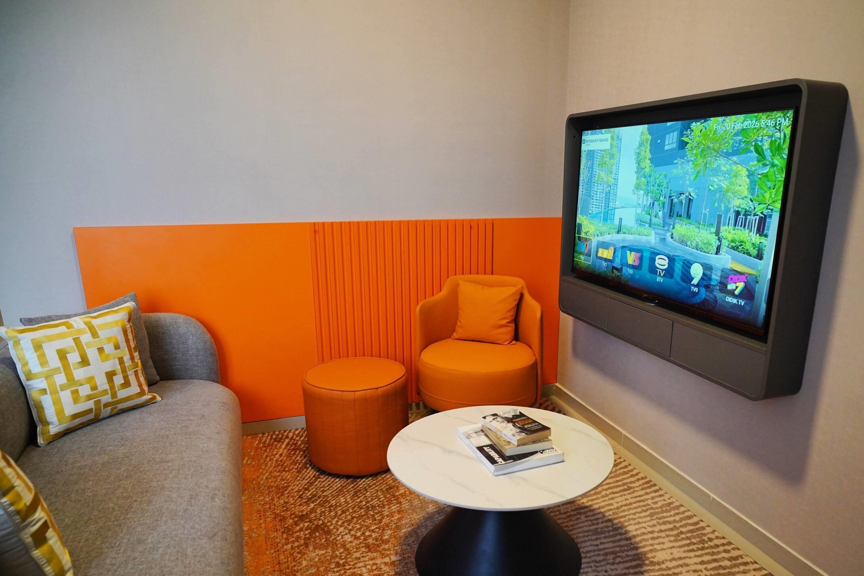 Una sala de estar moderna con un sofá gris, un reposapiés naranja y un televisor de pantalla plana montado en la pared.